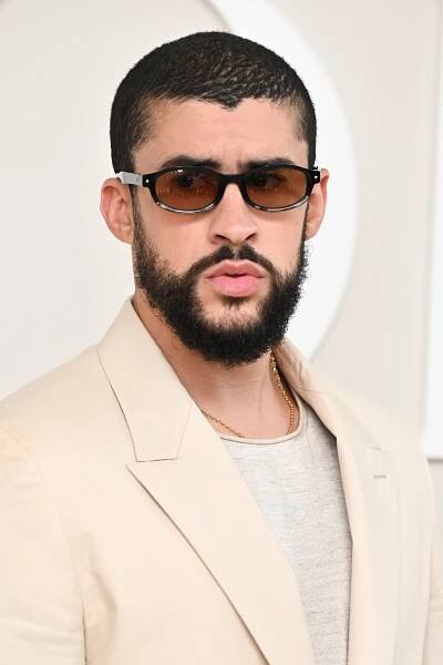 Person with short hair and beard wearing sunglasses and a tailored suit poses confidently
