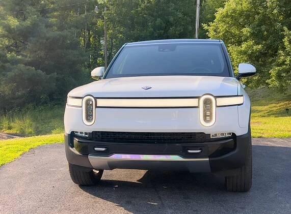 A white Rivian R1S in the late afternoon sun, seen head-on
