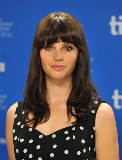 a woman with long hair wearing a polka dot dress and looking at the camera while standing in front of a blue backdrop