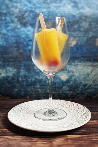 Two mimosa popsicles upended in a clear wine glass.