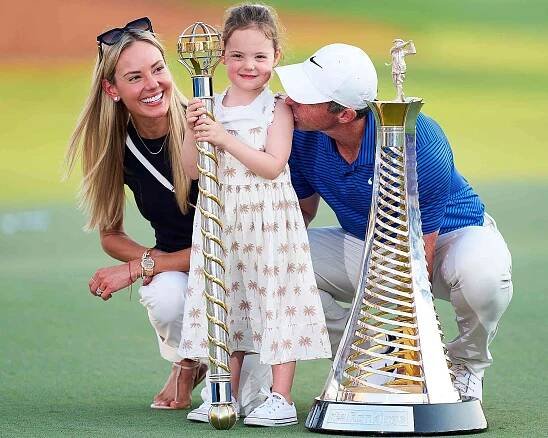 : Rory McIlroy of Northern Ireland poses with his Wife, Erica Stoll and Daughter, Poppy McIlroy alongside the DP World Tour Championship trophy and the Race to Dubai trophy on the 18th green following victory on day four of the DP World Tour Championship 2024