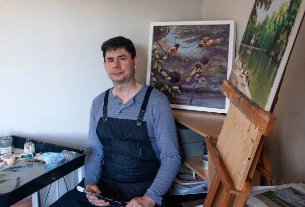 Artist Gary Martin sitting at easel surrounded by artwork