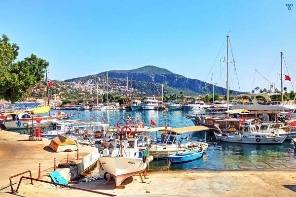 Kalkan harbour with small fishing boats in the foreground and larger wooden gulets anchored in deeper water.