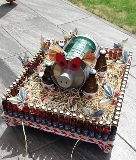 a pig made out of beer bottles sitting on top of a wooden tray filled with straw