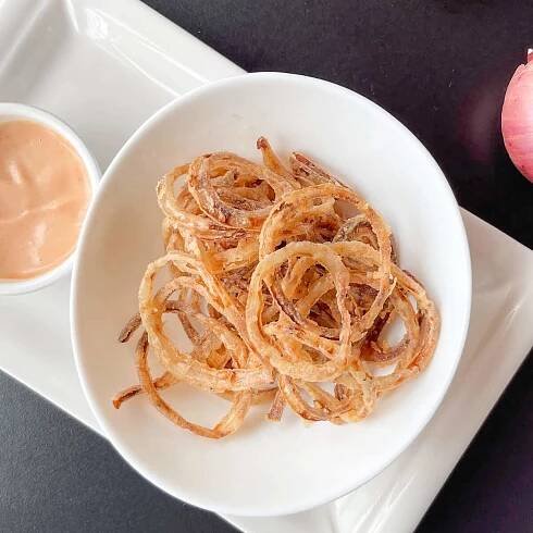 Crispy fried onion rings on a white oval bowl.