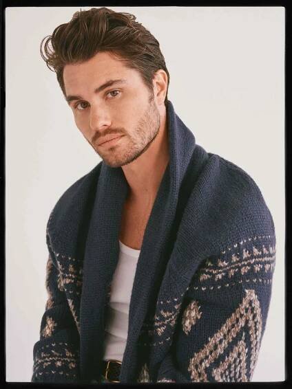 Chase Stokes wearing a blue shawl sweater and looking at the camera.