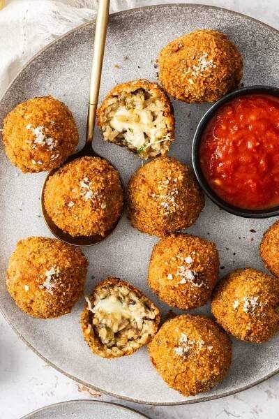 Top down view of a grey plate with 10 mushroom arancini with one split in half.
