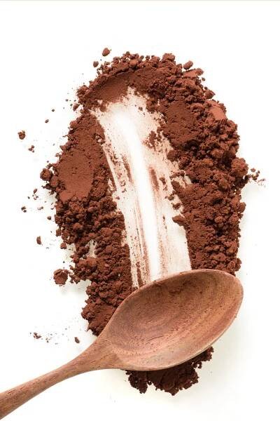 This is an image of cocoa powder being smeared on a white surface. A wood spoon rests in the powder, leaving a trail of powder brushed away behind it.