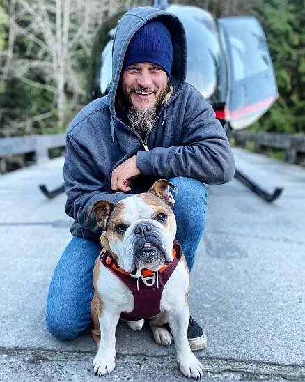 a man sitting on the ground next to a dog with a hood over it's face