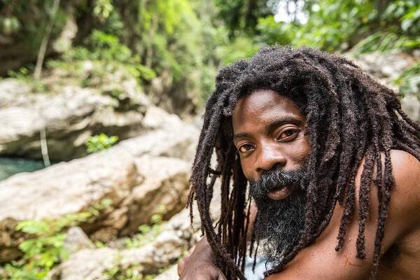Rastafari Man with long beautiful dreads in Jamaica at a swimming hole and water fall on the Marley Coffee planation, owned by Rohan Marley, the Son of legend Bob Marley, in the Blue Mountains of Jamaica.  Lifestyle photographer, industrial photographer and advertising photographer.  Short depth of field, shallow focus.
