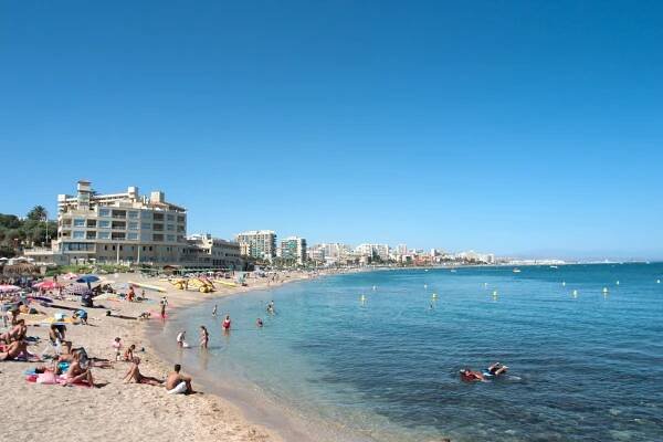 Beach scene in Benalmadena Costa, Spain, with people swimming and relaxing on the sand.