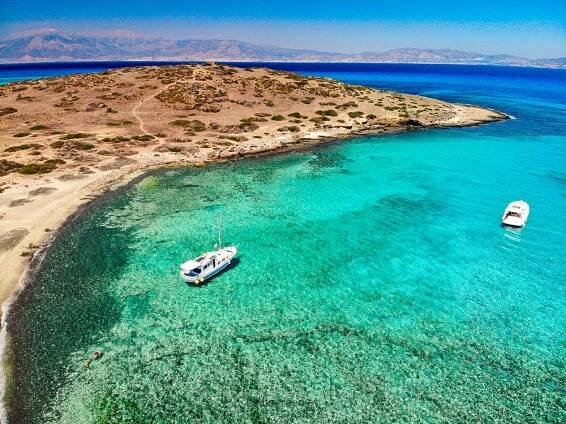 Turquoise waters and boats near a serene sandy beach on Chrissi Island, Crete, Greece.