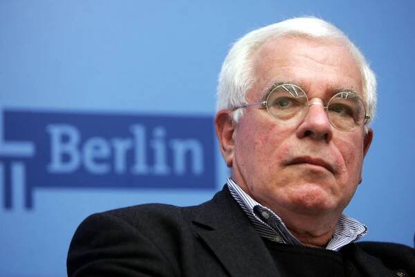 white man, white hair, thin-rimmed glasses, Berlin sign in background