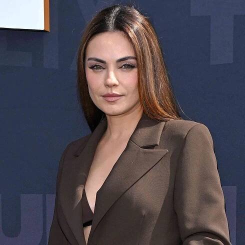 Mila Kunis posing at a formal event, wearing a professional outfit