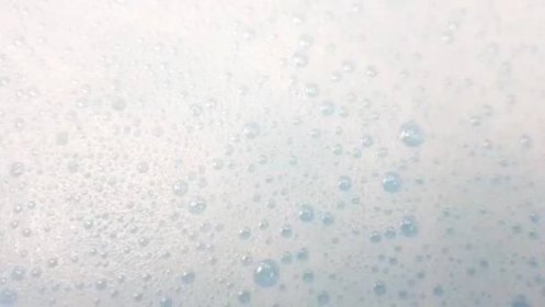 Bílá pěna s bublinkami praskající v čiré modré vodě, detailní záběr — Stock záběr
