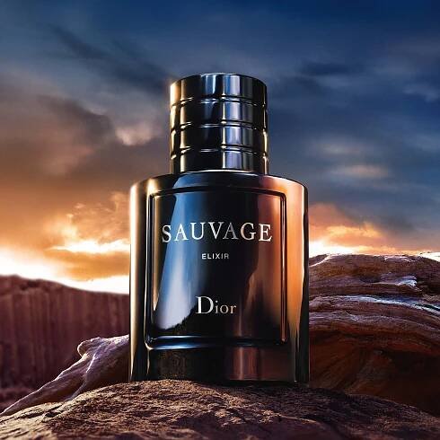 A bottle of Dior Sauvage Elixir perfume set against a dramatic sunset and rocky landscape.