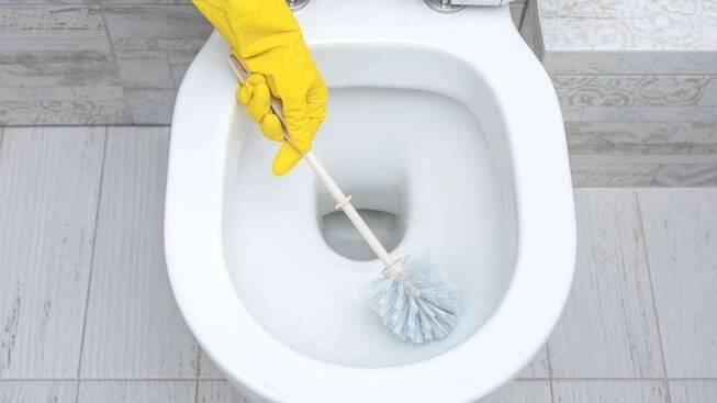 Gelber Handschuh hält Toilettenbürste in einer WC-Schüssel