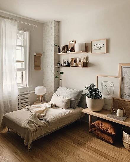 a bedroom with white brick walls and wooden flooring is pictured in this image, there are shelves on the wall above the bed