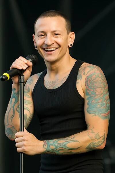 Chester Bennington se usmívá, v ruce drží stojan s mikrofonem a dívá se do publika, na sobě má černé tílko, bez brýlí – VytvořSiPotisk.cz