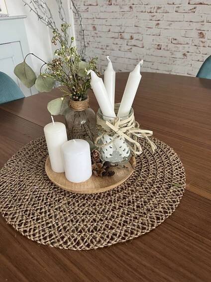 a wooden table topped with candles and vases on top of a woven place mat