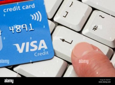 Contactless Visa credit card on a keyboard with a person's finger pressing enter key to buy online using Visa. Internet shopping concept. England UK Stock Photo