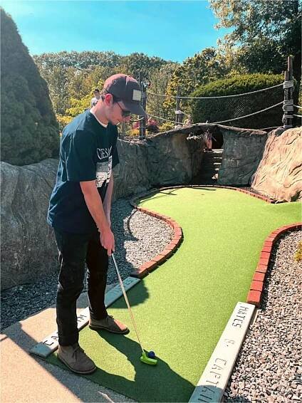 Person playing mini golf on green course with rocky landscape background
