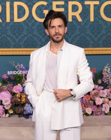 Jonathan Bailey posing at a "Bridgerton" Netflix event, standing in front of floral decor