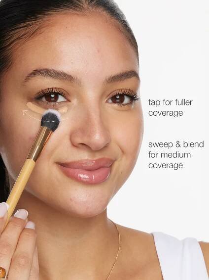 Woman applying makeup with a brush on her face, demonstrating coverage techniques.