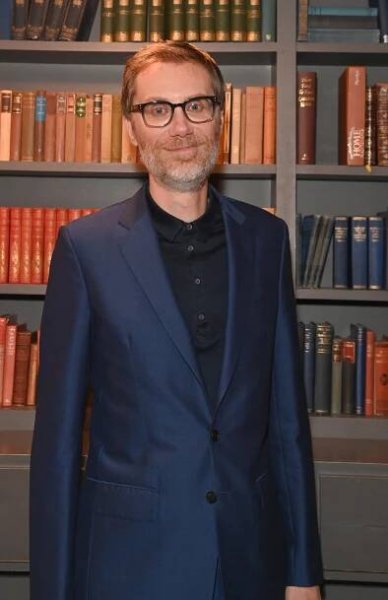a man in a suit stands in front of a bookshelf with a book called home on it
