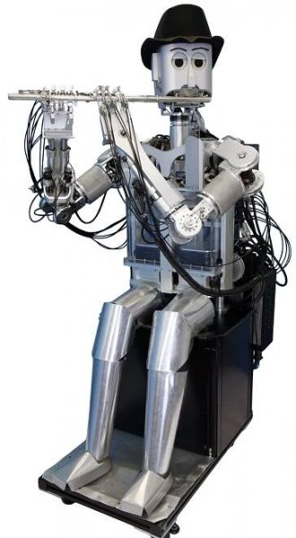 A seated silver humanoid robot whose torso and arms highlight many black wires wears a black hat and plays a flute against a white background.