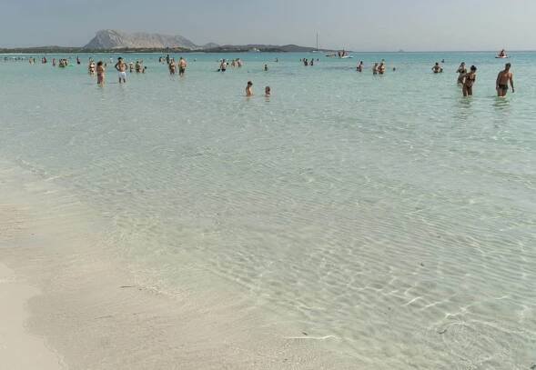 People wading in the water at a beach -- the water is very pale aquamarine and is shallow far out.