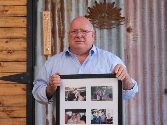 A man wearing a blue shirt holds a photo frame with photos inside 