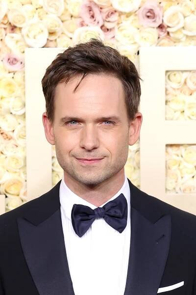 Patrick J. Adams in a tuxedo with a bow tie stands in front of a floral backdrop