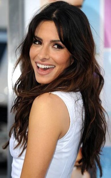 a woman with long dark hair smiling at the camera and wearing a white tank top