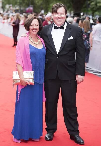 Mary Roscoe brings a vibrant splash of color in a cobalt blue maxi dress, pink shawl, and metallic clutch as she joins husband Jeremy Swift, dapper in a classic black tux, on the red carpet for BAFTA’s Downton Abbey celebration in Richmond