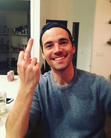 a man sitting at a table with his hand up in the air, smiling and making a peace sign