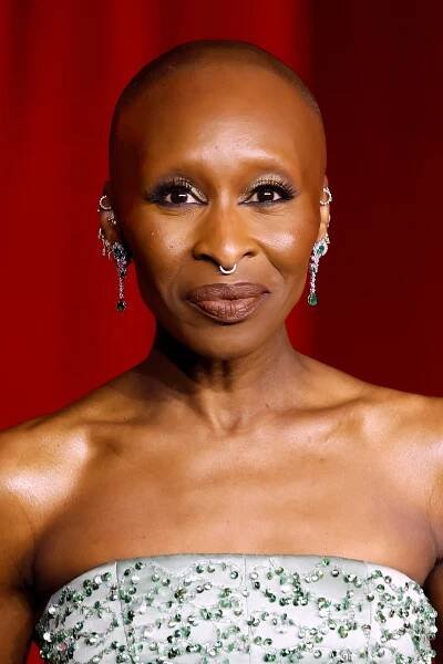 Cynthia Erivo wearing elegant strapless gown and long earrings, standing against a red background