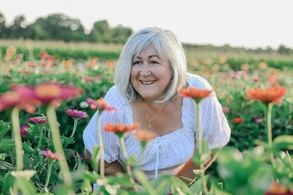 Tammy with White Lilac Farmhouse in a field of zinnias.