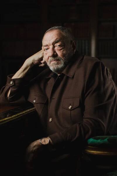 Dick Wolf, wearing a brown shirt, sitting at a desk.