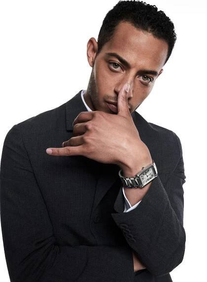 Image may contain Human Person Suit Coat Clothing Overcoat Apparel and Wristwatch