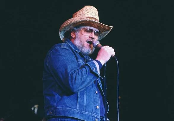 Canadian entertainer, Ronnie Hawkins, wearing cowboy-type clothing and singing to live audience.