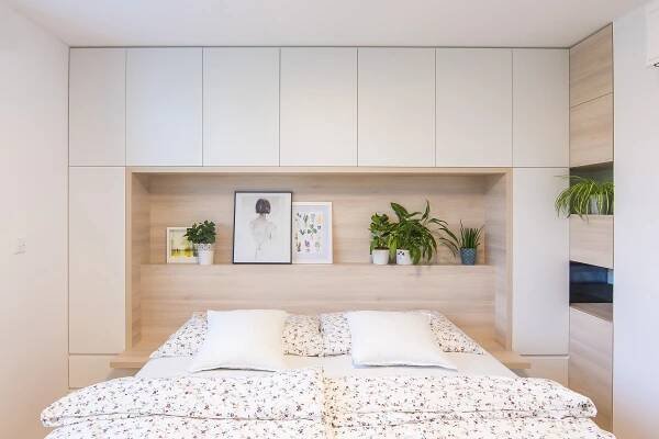 there is a bed with white sheets and pillows in the room that has potted plants on the wall