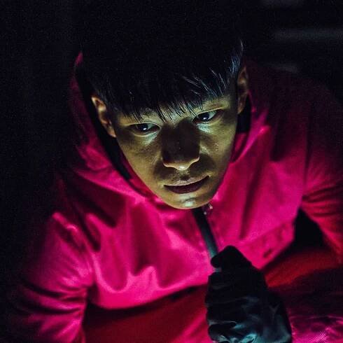 Wi Ha-joon as Hwang Jun-ho in a pink suit with a glow on his face in a still from squid game season 1