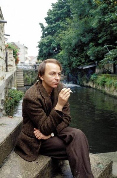Michel Houellebecq in 1995 smoking a cigarette next to a body of water.