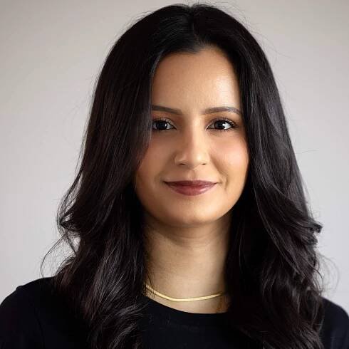 A woman with long dark hair is wearing a black shirt and a gold necklace.