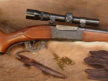 A Savage Model 99 lever action rifle and other hunting gear and bullets on an animal hide.
