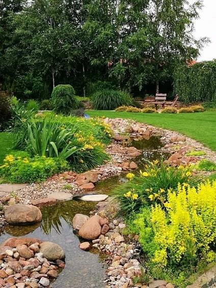 a small stream running through a lush green park filled with lots of flowers and trees