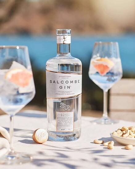 Salcombe Gin bottle with cocktail garnished with grapefruit, two glasses filled with ice, and cashews on a table, showcasing Salcombe Distilling Co.'s premium gin for social media marketing.