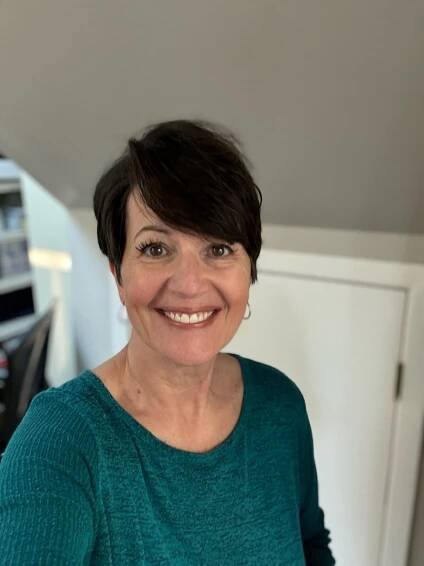 A woman in a green shirt is smiling for the camera.