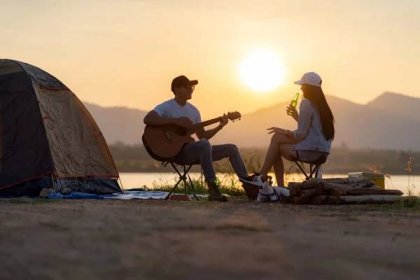 Mladý dospělý asijský pár hrající na kytaru a pijící pivo u svého stanu tábořiště při západu slunce. Kempování výlet se psem outdoorové aktivity kemp koncept. — Stock obrázek
